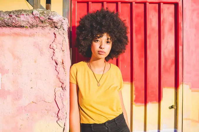 Portrait of young woman with afro hairdo leaning against a wall