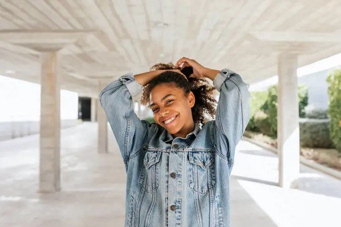 Portrait of young smiling woman pulling her hair up in parking