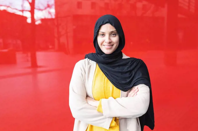 Portrait of smiling young woman wearing hijab in front of red glass pane