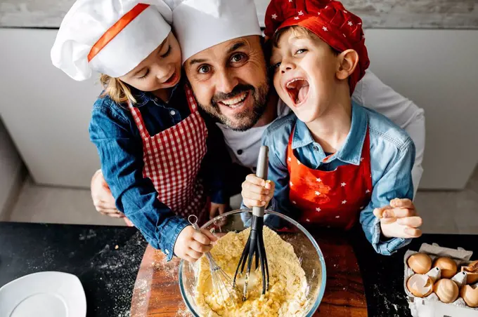 Portrait of happy father with two kids preparing dough in kitchen at home