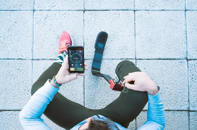 Disabled athlete with leg prosthesis having a break from exercising checking cell phone with data