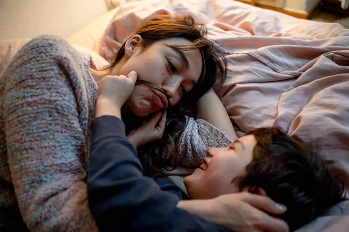 Mother and little son lying together on bed having fun