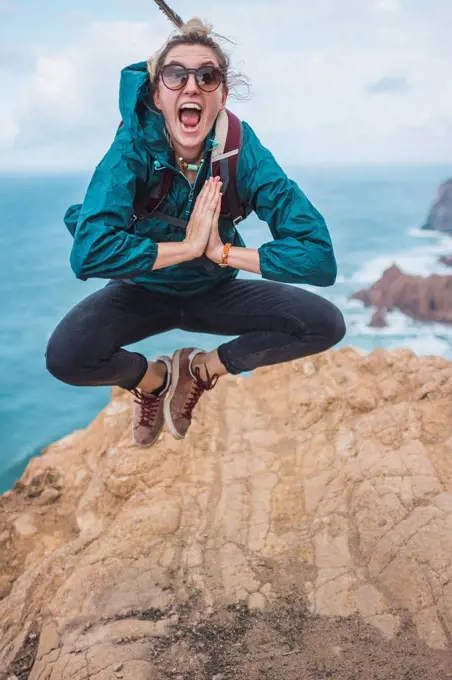 Portugal, Lisbon District, Sintra, Portrait of female hiker jumping at edge of Cabo da Roca cliff