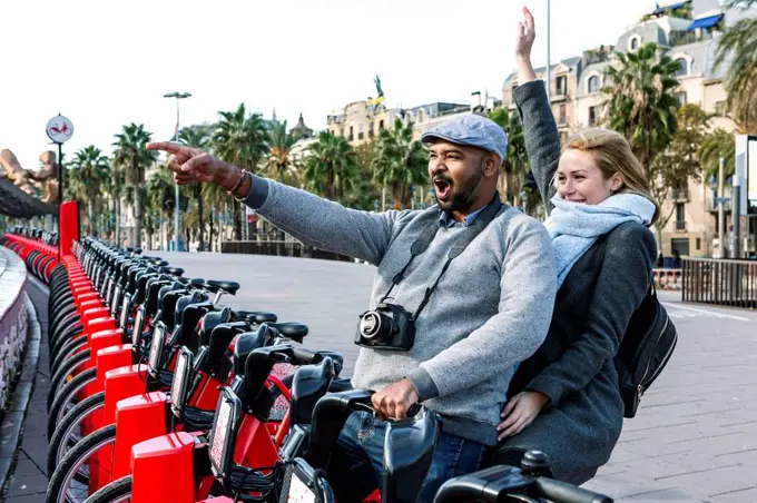 Happy couple at bike share stand in city, Barcelona, Spain