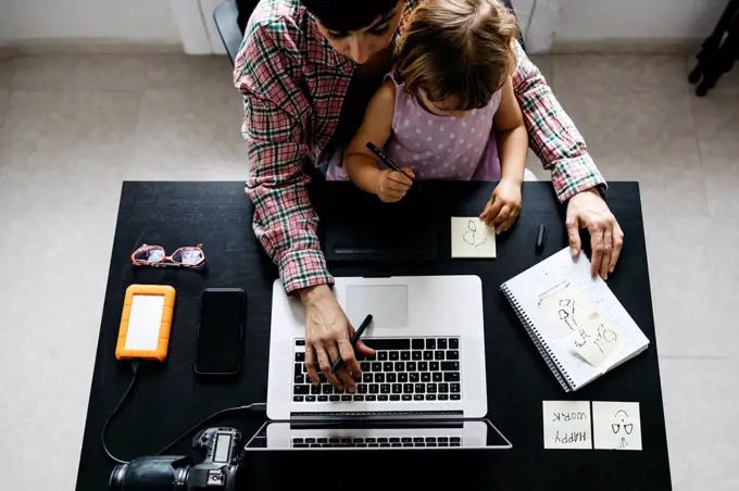 Mother working at home with her daughter, from above