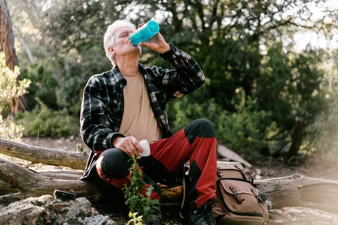 Hiker with backpack having a break drinking water from bottle