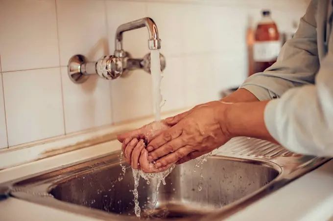 Close-up of a woman washing her hands with soap and water at the kitchen basin