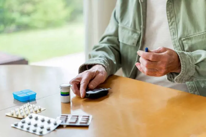 Midsection of retired diabetic senior man examining himself while sitting at table