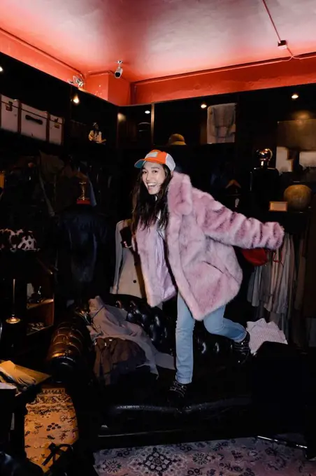 Cheerful woman wearing fur jacket standing on sofa at thrift store