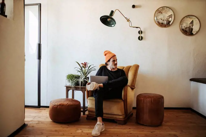 Man with laptop sitting on armchair at home