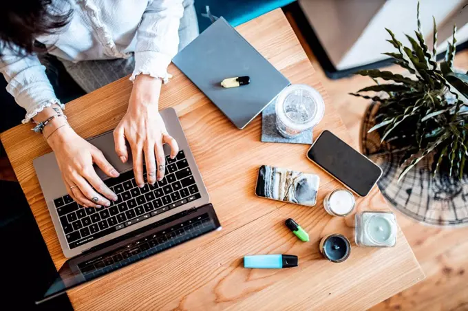 Crop view of young woman working on laptop at home, top view