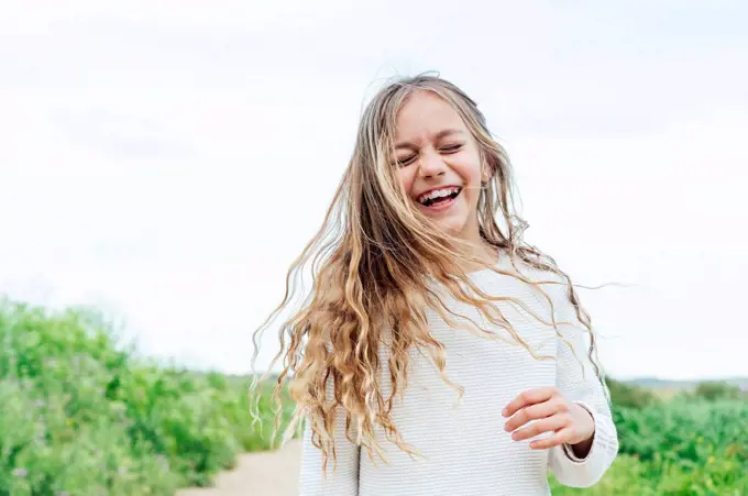 Carefree blond girl standing with eyes closed against sky