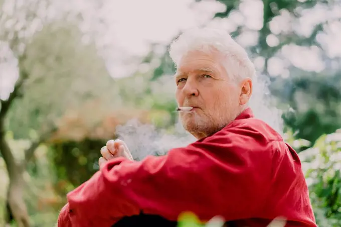 Retired senior man smoking marijuana while sitting at orchard