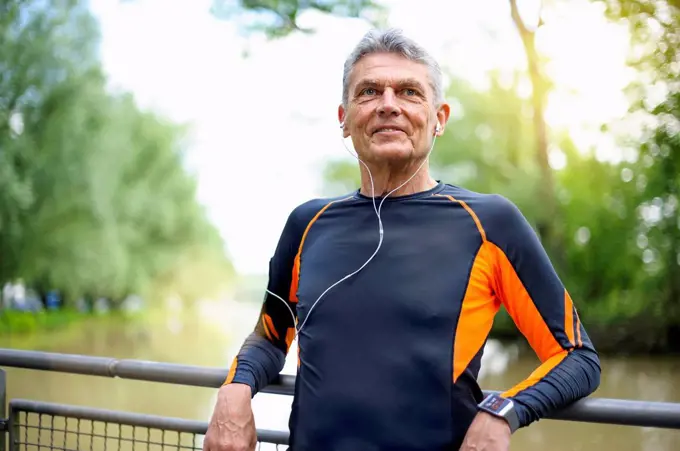 Retired senior man looking away while smiling against railing in park