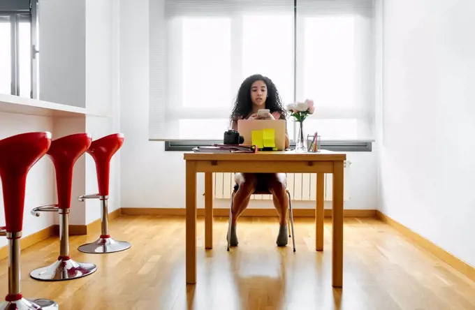 Young woman working from home using smartphone and laptop