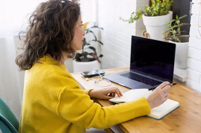 Woman working at desk in home office taking notes