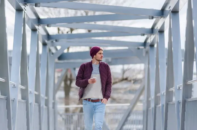 Young man walking on a bridge with earbuds and smartphone