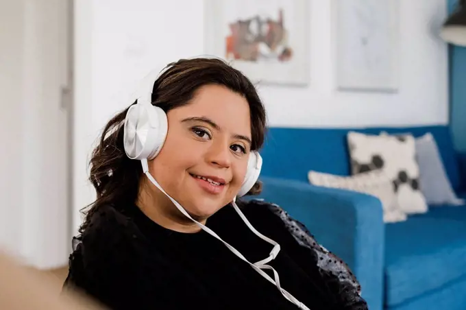 Happy woman with down syndrome listening music while relaxing in living room