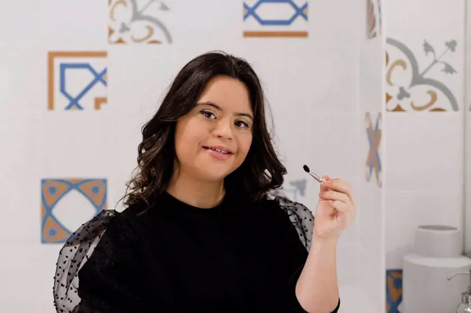 Confident woman with down syndrome holding make-up brush in bathroom at home