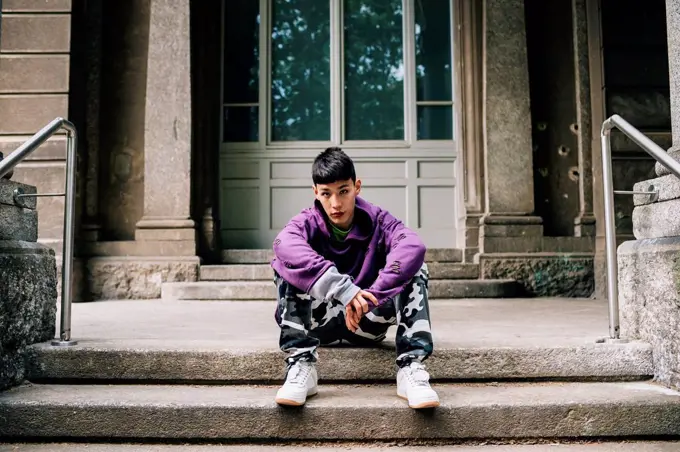 Cool confident man sitting on steps against house