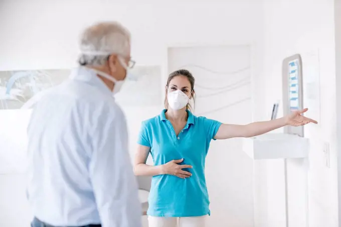 Senior man meeting his femal physiotherapist at the reception, wearing face masks