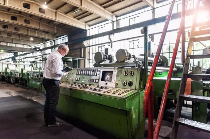 Senior businessman examining a machine in a factory hall