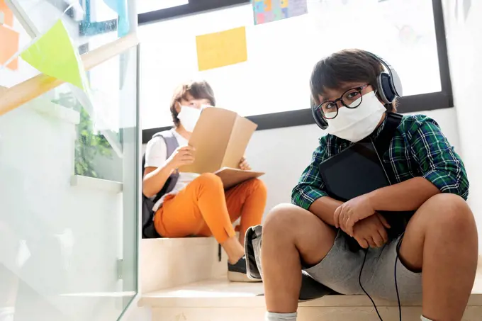 Boys wearing masks sitting at distance on steps in school