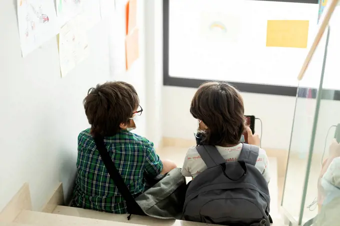 Boys wearing masks talking while sitting on steps in school