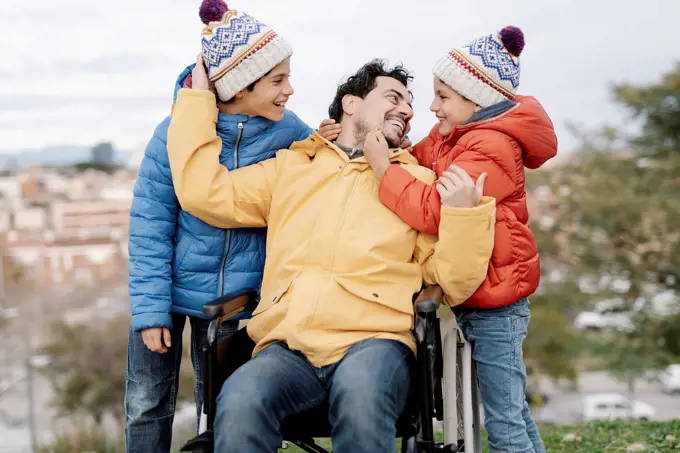 Loving father embracing sons while sitting on wheelchair in park