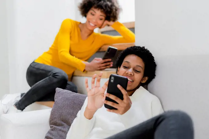 Two young women relaxing at home using their smartphones