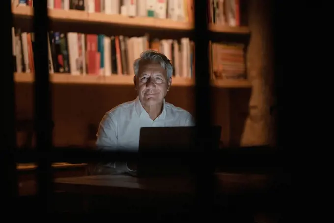 Senior businessman sitting in office, working late, smiling