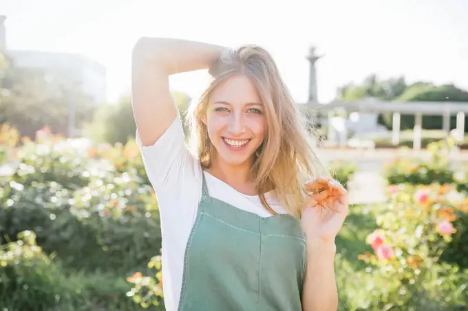 Portrait of happy young woman in public garden at backlight