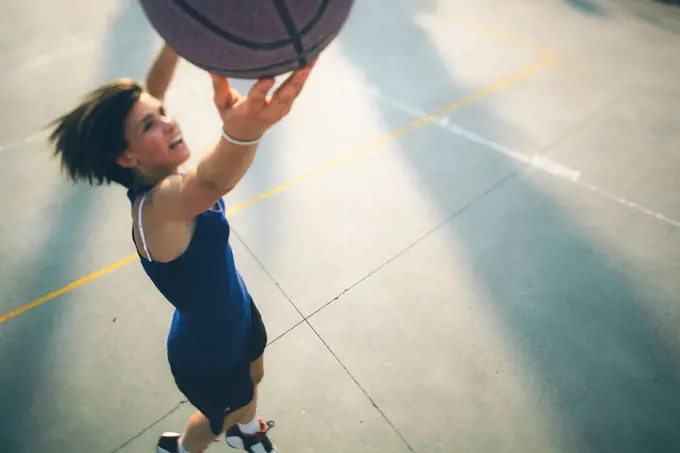 Teenage girl jumping while practicing basketball on court