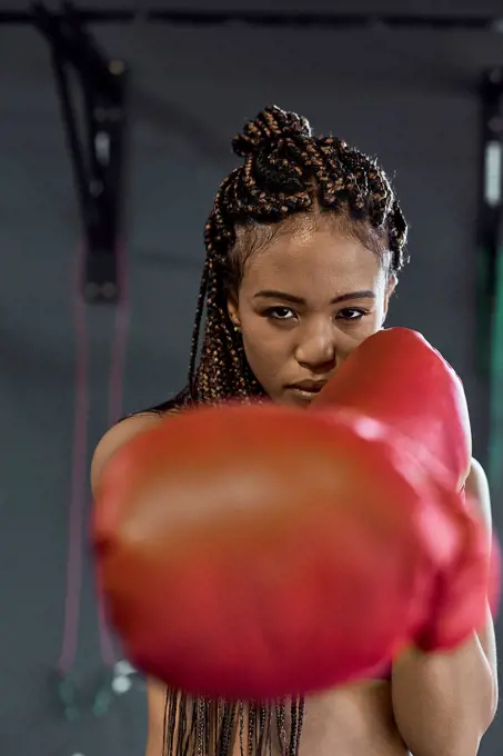 Confident young woman wearing red boxing gloves exercising in gym