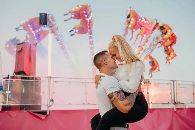 Romantic man carrying girlfriend while standing at amusement park