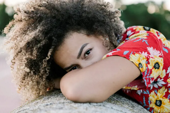 Confident young woman leaning on retaining wall during sunny day