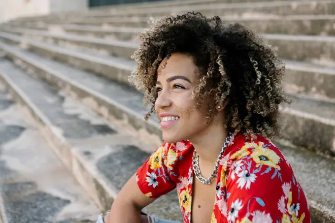 Thoughtful young woman smiling while sitting on steps during sunny day