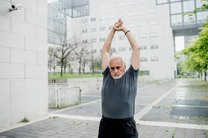 Senior man with arms raised exercising against building in city