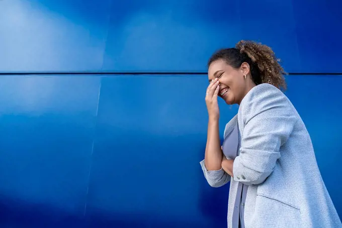 Laughing businesswoman in front of blue wall