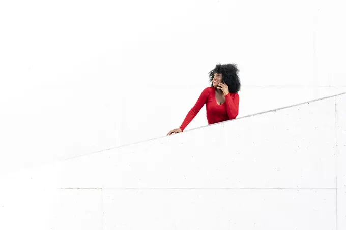 Young woman with afro hair using smartphone on white ramp