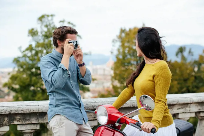 Young man photographing girlfriend sitting on Vespa