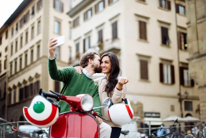 Romantic man taking selfie while kissing woman in Florence city, Italy