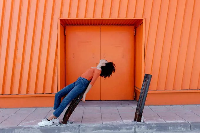 Young woman leaning on damaged metal by orange door