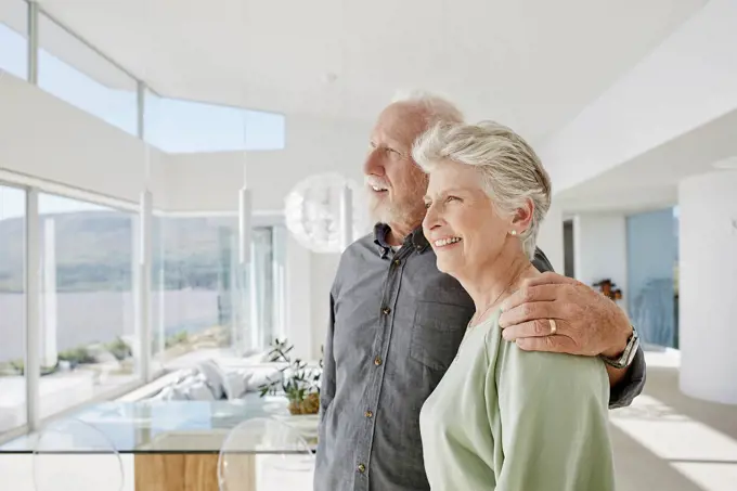 Happy senior couple in luxury beach house looking out of window