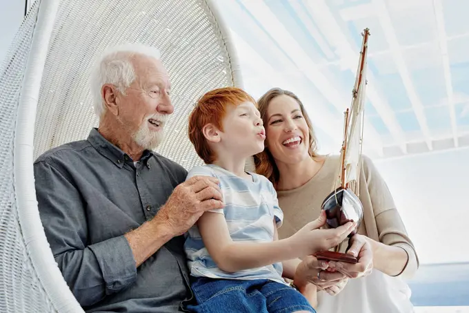 Happy grandfather, mother and son with model sailing ship in hanging chair