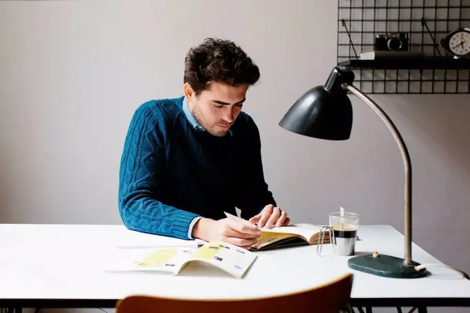 Male architect reading book while sitting at desk in office