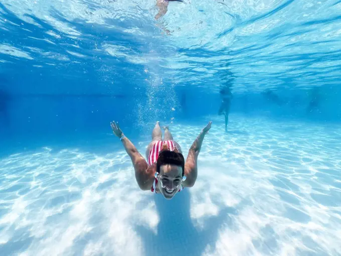 Smiling woman swimming underwater in pool at tourist resort