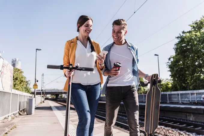 Smiling woman showing smartphone to male friend while walking at railroad station