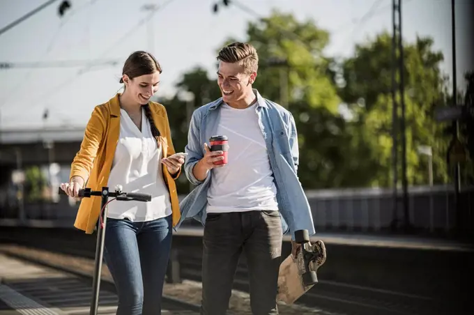 Young woman showing smart phone to male friend while walking at railroad station