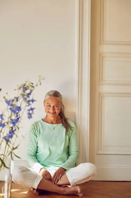 Smiling woman with cross-legged sitting on floor against wall at home